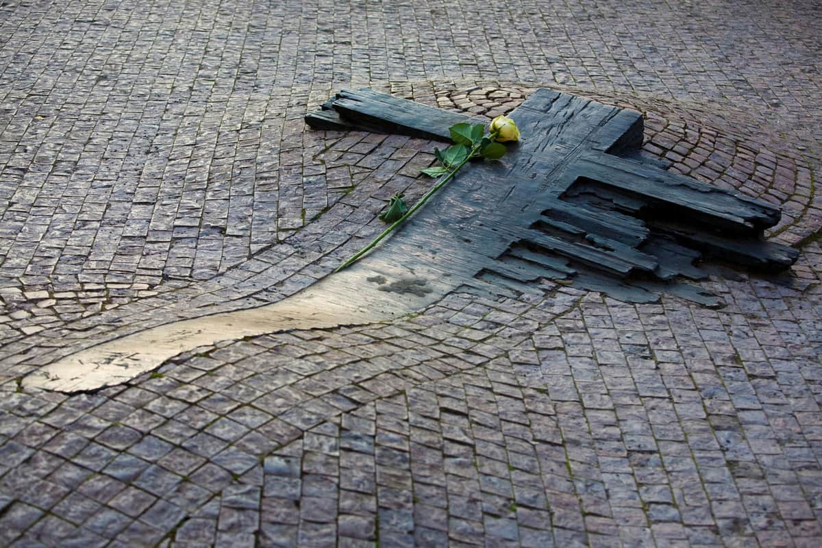 Musée du communisme & visite de la Prague communiste Une rose jaune sur un monument en pierre en forme de croix encastré dans un chemin pavé.