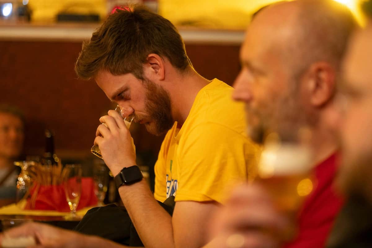 St. Pauli Beer Tour - Beer and District A man in a yellow shirt sniffs a drink glass while sitting indoors. Another person is partially visible in the foreground.