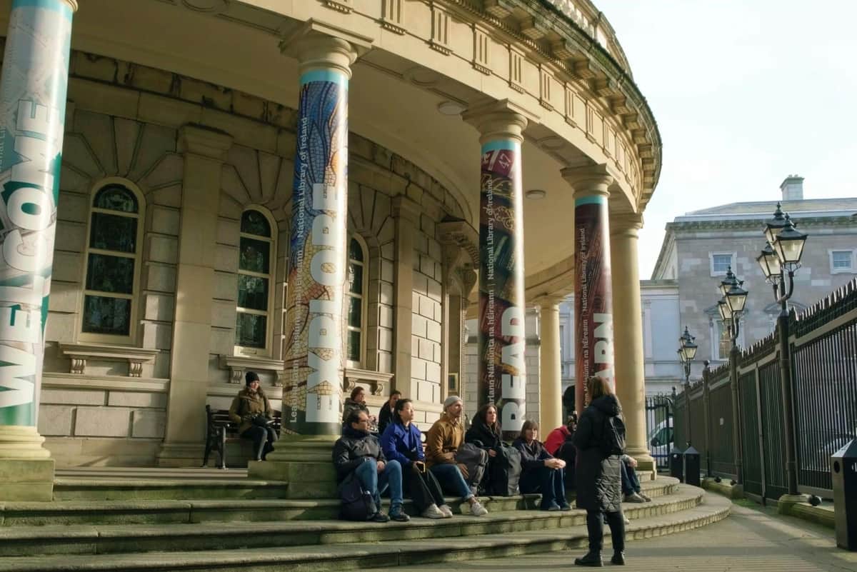 People sitting and talking on the steps of a building with large columns featuring the words "EXPLORE," "READ," and "LEARN."