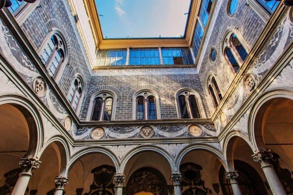 Palazzo Vecchio: Skip The Line Ticket + Guided Tour Interior courtyard of a historic building with arched windows, intricate stonework, and an open view of the blue sky above.