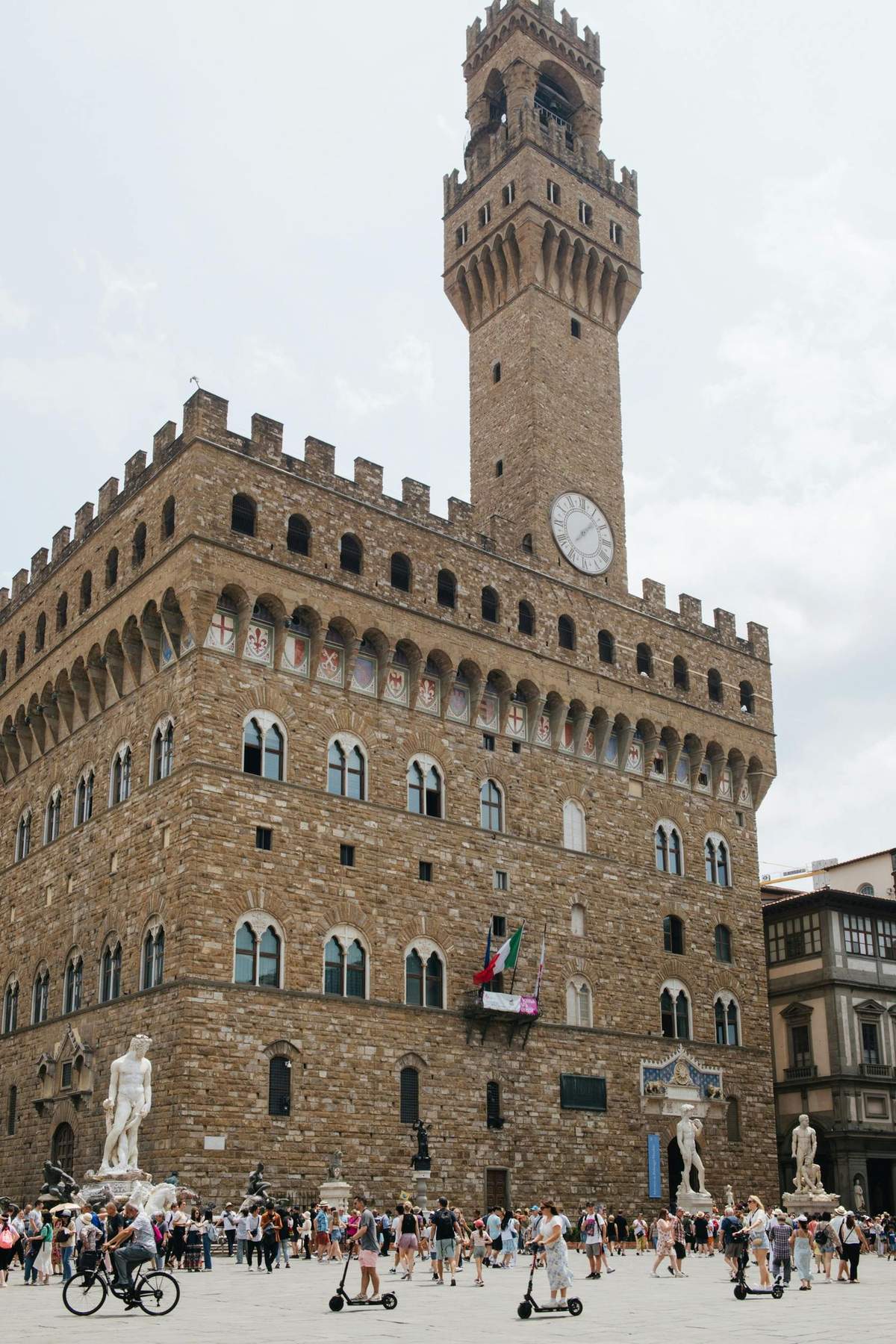 Pisa and Florence: Day Trip from Livorno A large, historic stone building with arched windows, a clock tower, and a statue in front. Italian flags hang from a balcony.