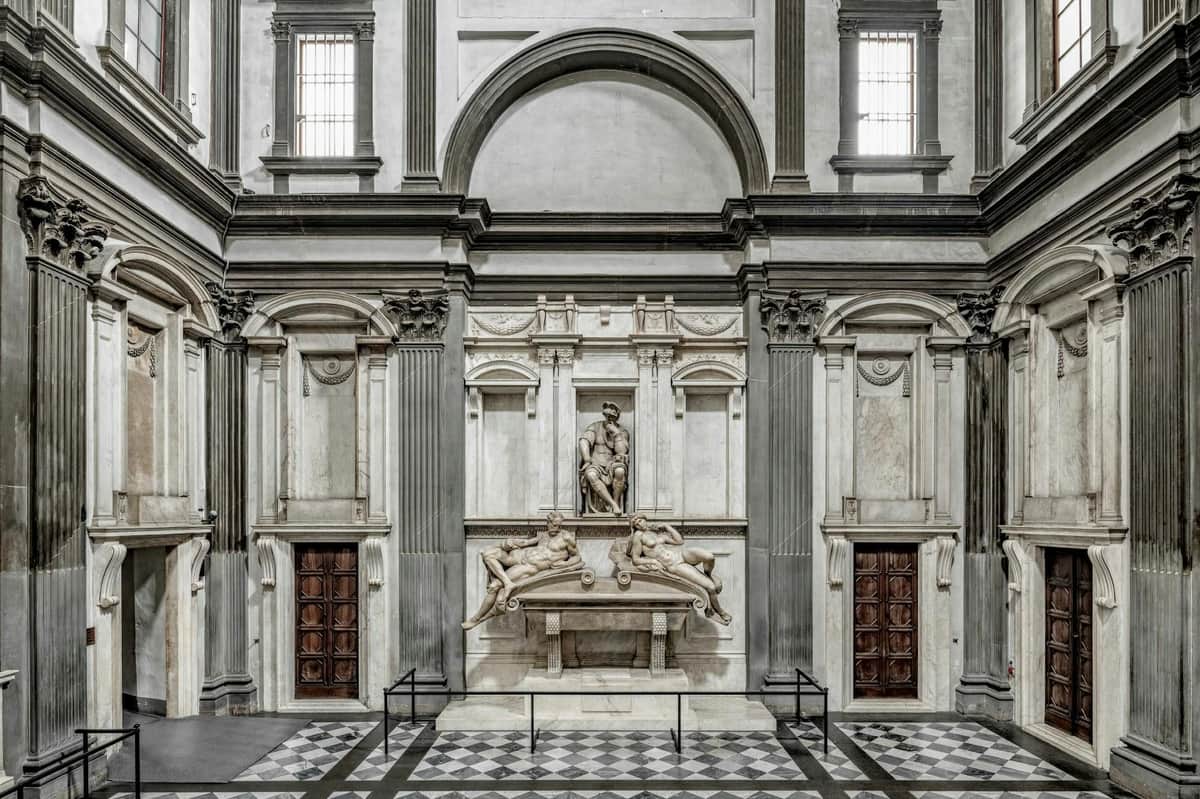 The Medici Chapel: Guided Tour Interior of a historical building with decorative architecture, statues, and two wooden doors on either side.