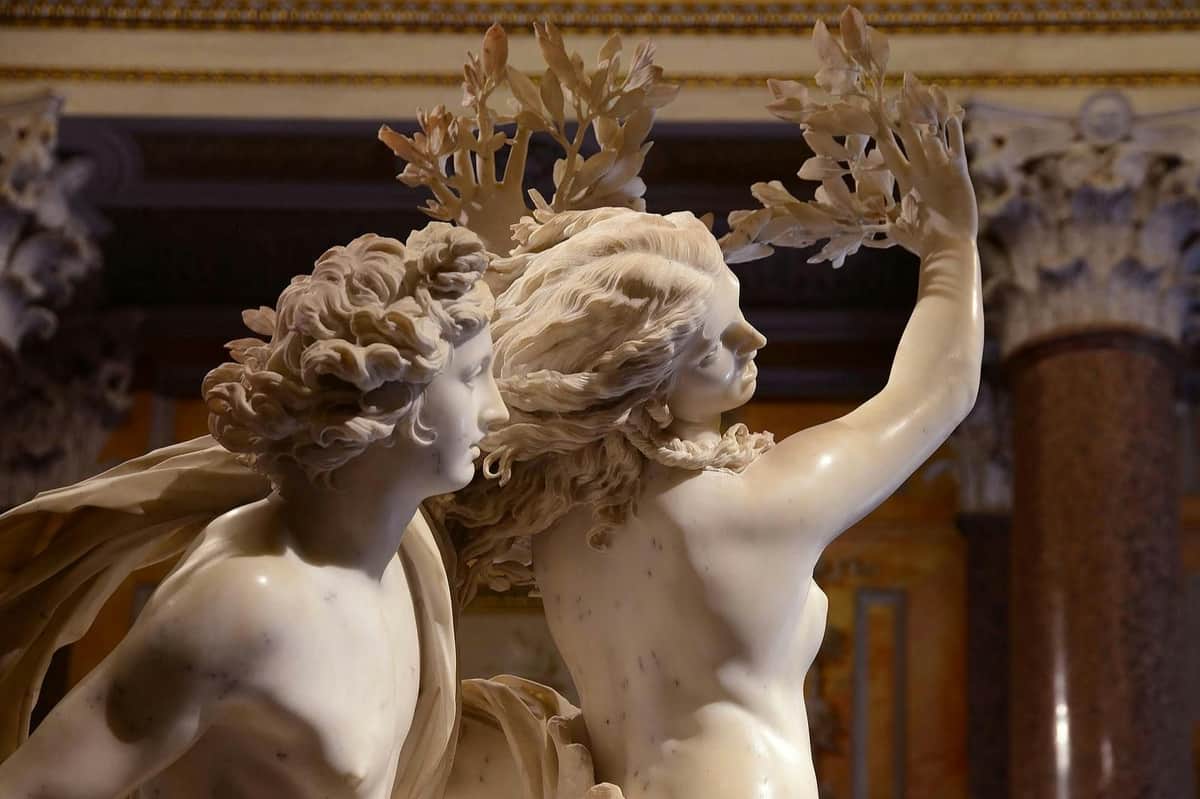 Galerie Borghèse : Billet coupe-file + Visite guidée en petit groupe Une sculpture en marbre représentant deux personnages, dont l'un tend les bras vers le ciel, ses bras étant des branches, sur fond d'intérieur richement décoré.