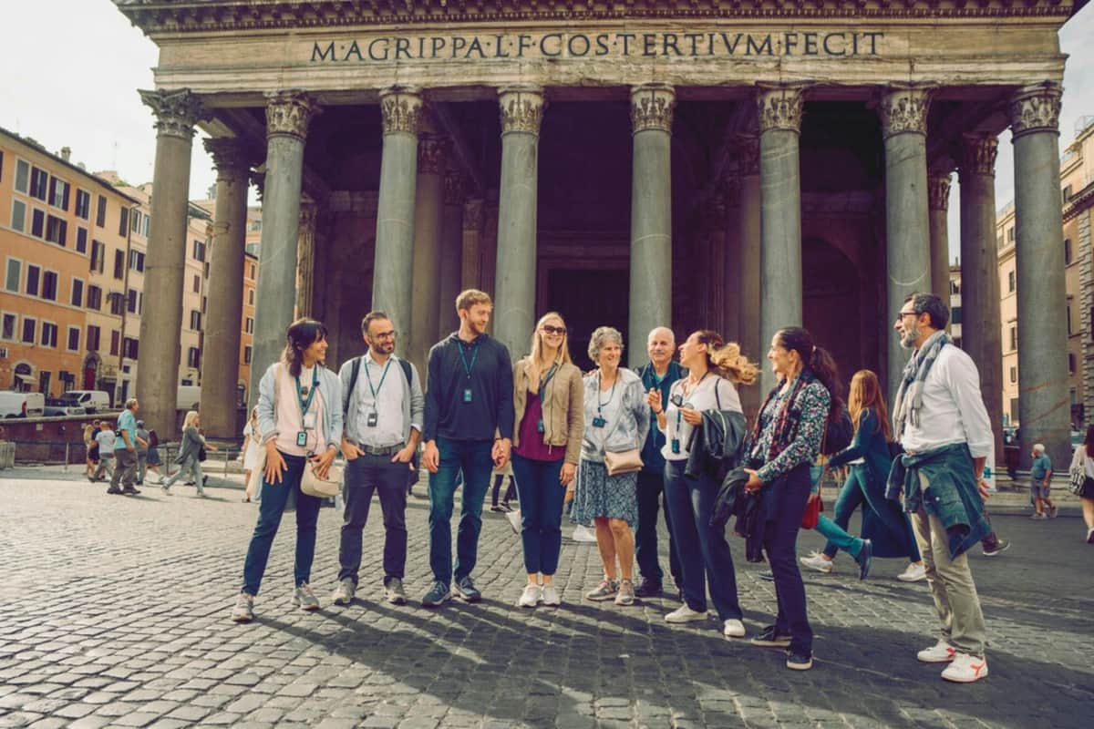 Rome : Visite guidée à pied + visite du Panthéon Groupe de touristes avec audioguides devant un bâtiment ancien avec de grandes colonnes et une inscription.