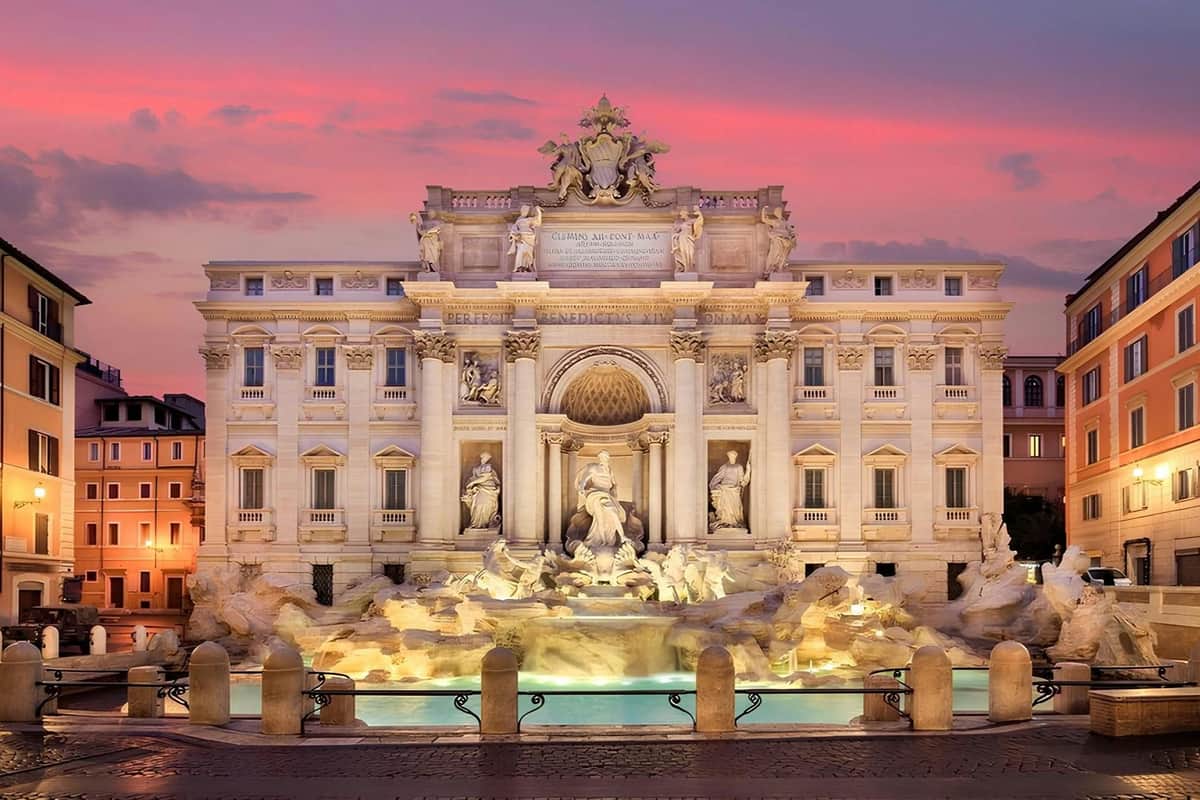 ローマのトレビの泉は、夕暮れ時にライトアップされ、前景には華やかな彫刻と水のプールがあります。
