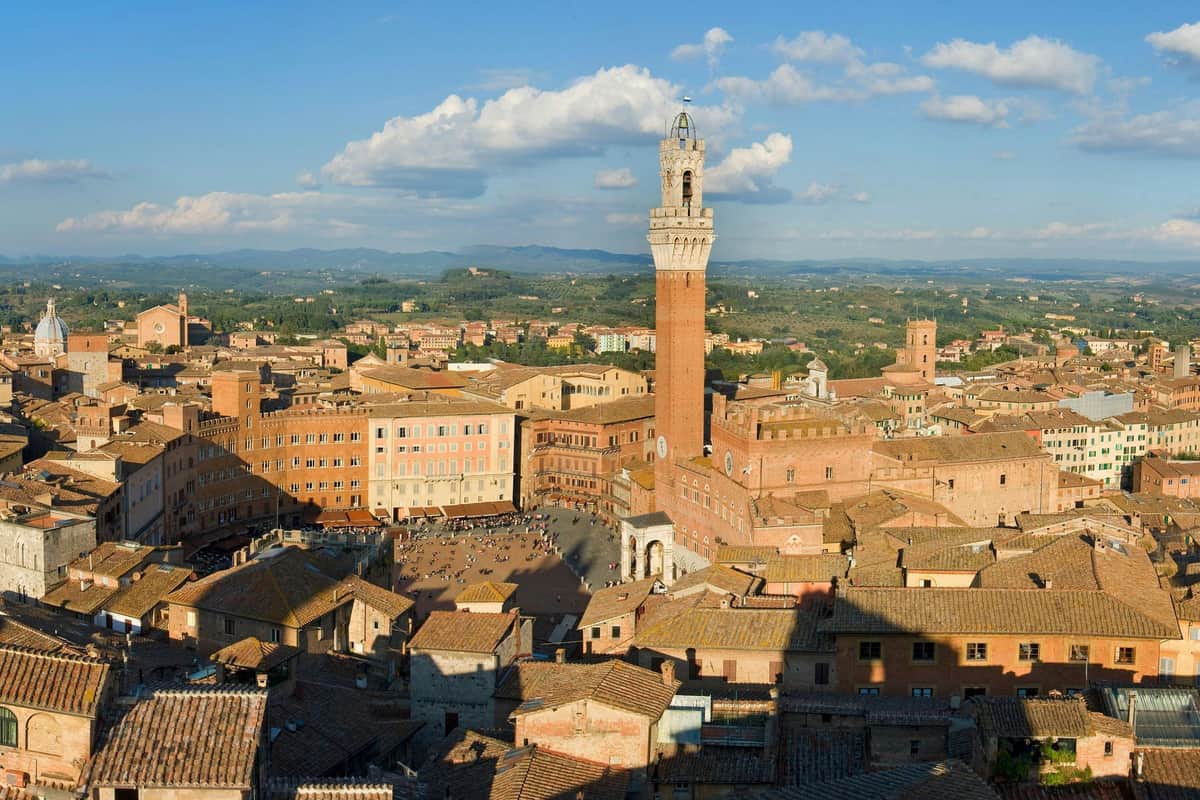 Paysage urbain de Sienne, en Italie, montrant la Piazza del Campo avec sa tour emblématique, entourée de bâtiments historiques sous un ciel bleu.