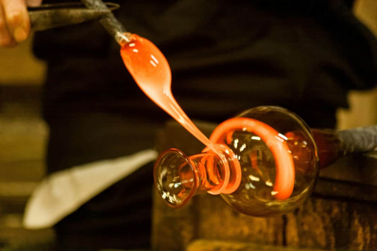 Murano: Private Glass Blowing Demo + Tour Close-up of glassblowing process with glowing orange molten glass being shaped and drawn from a furnace.