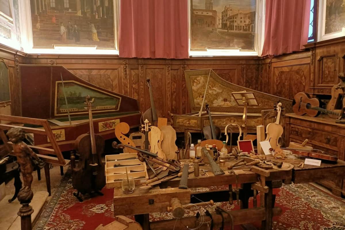 Music Museum & Baroque Concert A workshop filled with string instruments, including violins and harpsichords, surrounded by various woodworking tools and parts.