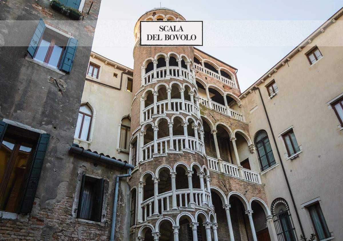 Venise : Visite guidée à pied de San Marco au Rialto + Spritz Un escalier en colimaçon à plusieurs étages avec des arcs blancs sur une tour en briques appelée "Scala del Bovolo", entourée de vieux bâtiments.