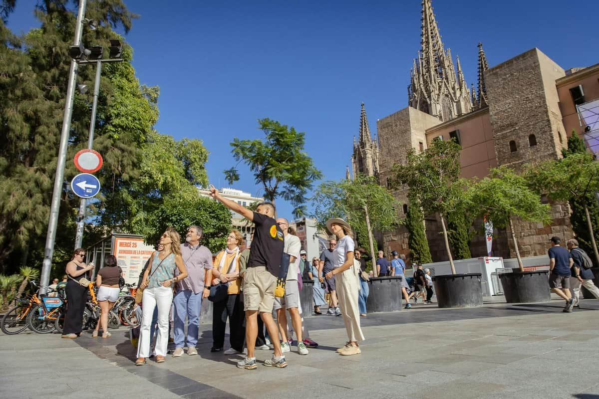 Barcelona: Historic Center Guided Walking Tour A group of people stand outdoors near trees and a church, with one person pointing as they appear to be on a tour.