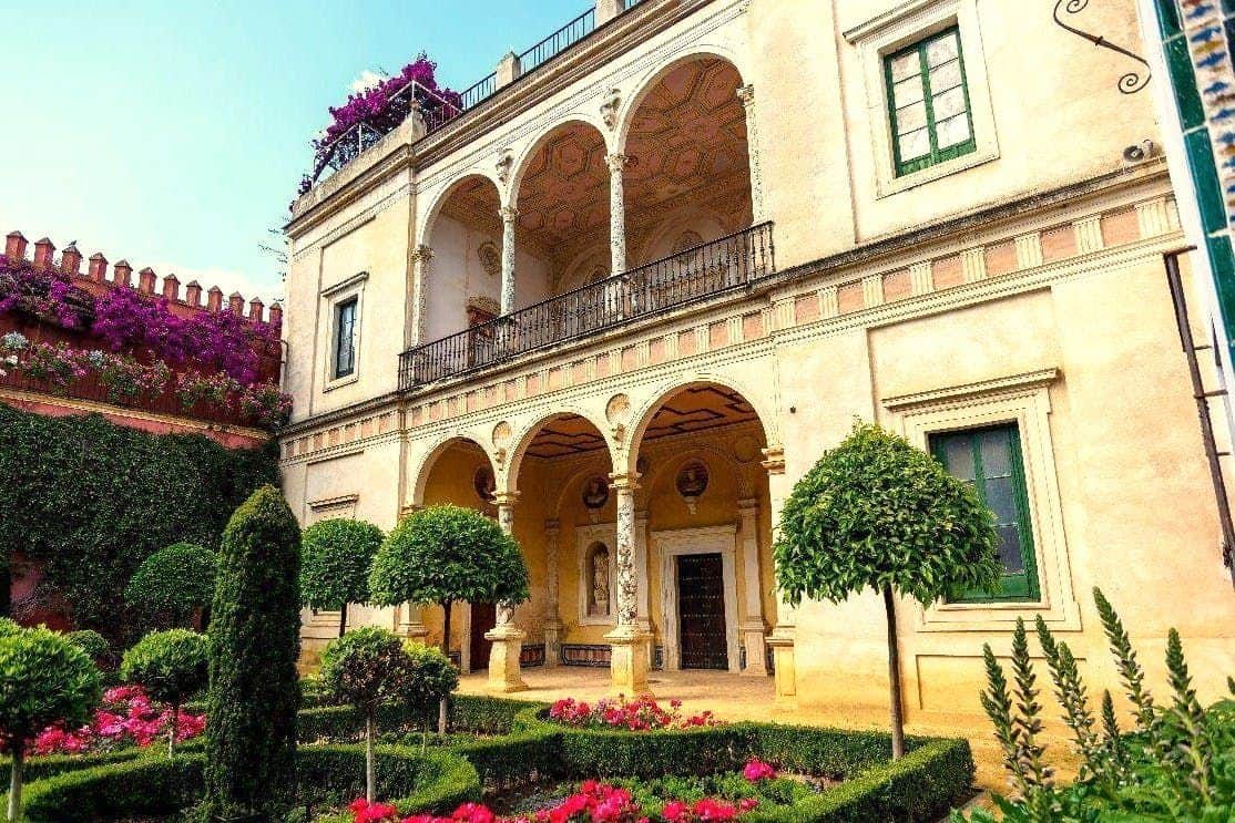 Palacio de las Dueñas & Casa de Pilatos : Visite guidée (Séville) Bâtiment orné de deux étages avec balcons en arc de cercle, jardin entretenu et fleurs colorées au premier plan.