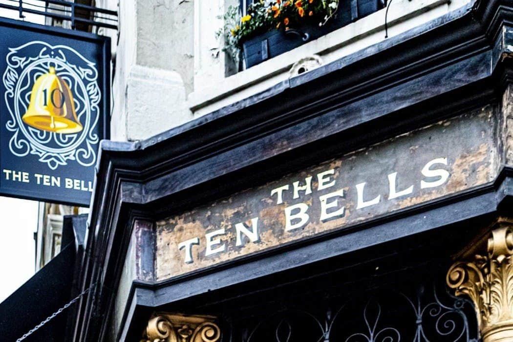 Londres : Visite guidée à pied de Jack l'Éventreur Une enseigne indiquant "Les dix cloches" au-dessus d'une porte, avec un bac à fleurs et des détails architecturaux ornés visibles.