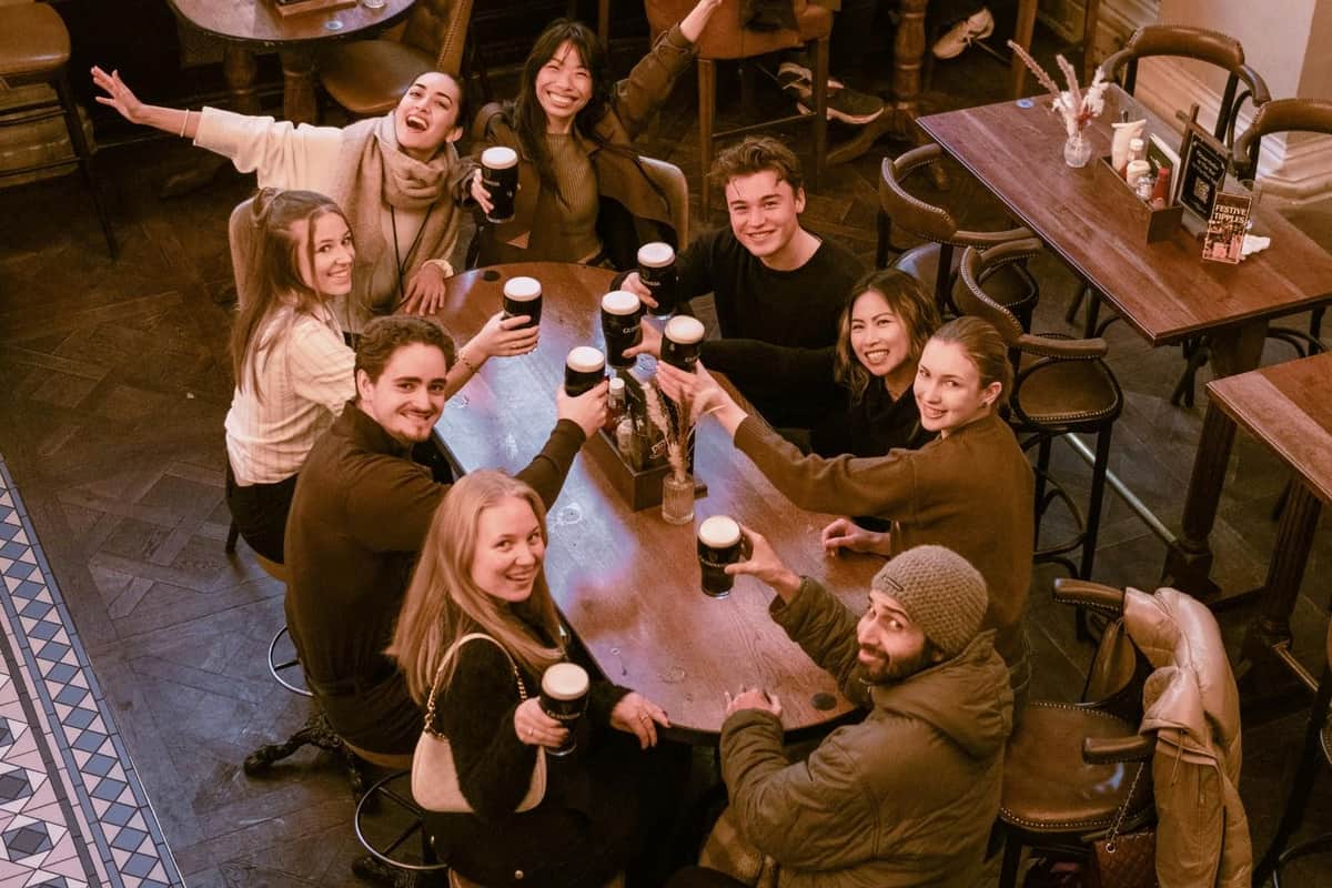 Londres : Visite guidée des pubs et tavernes Un groupe de personnes assises autour d'une table en bois dans un cadre confortable, brandissant des boissons et souriant joyeusement.