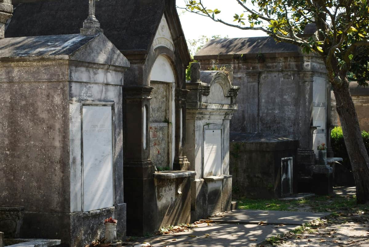 Garden District: Guided Walking Tour A row of above-ground tombs in a cemetery, with stone facades and greenery surrounding them under a sunny sky.
