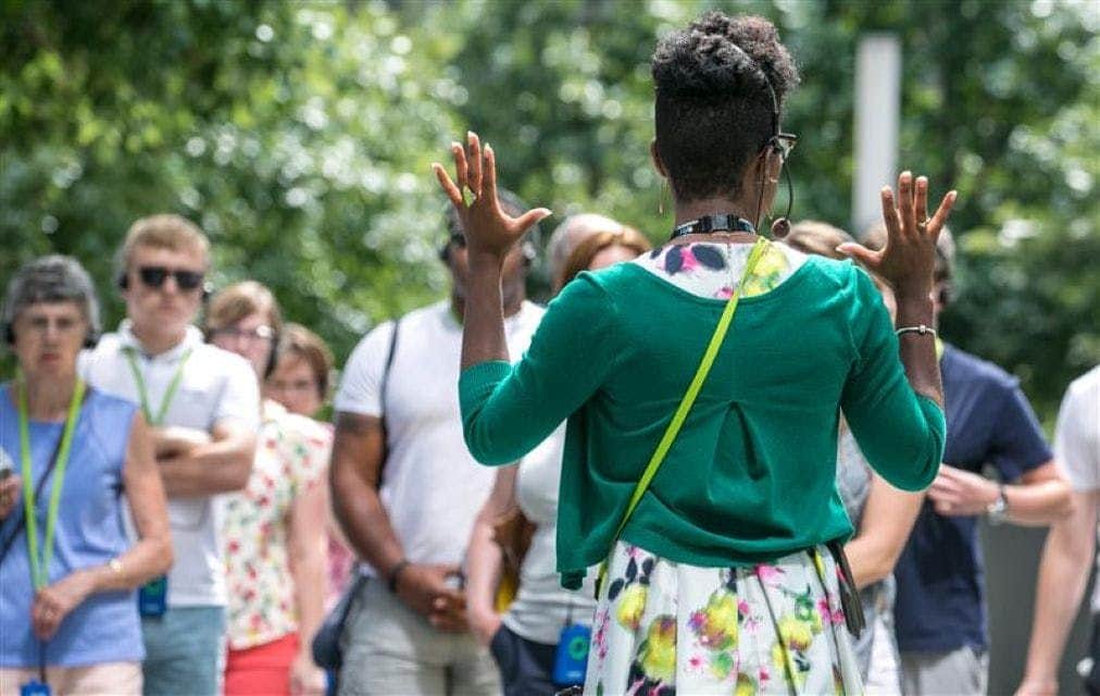 Place commémorative du 11 septembre : visite guidée Un groupe de personnes écoutant un guide qui fait des gestes de la main, en plein air, dans un cadre verdoyant et arboré.