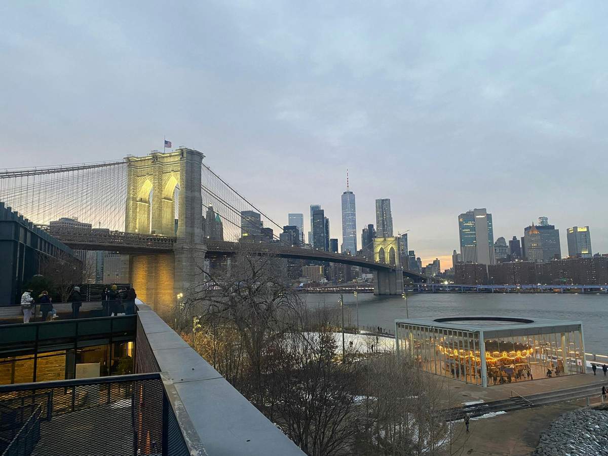 Brooklyn Heights, DUMBO, The Bridge Le pont de Brooklyn au crépuscule, avec les gratte-ciel de la ville en arrière-plan et un parc au premier plan.