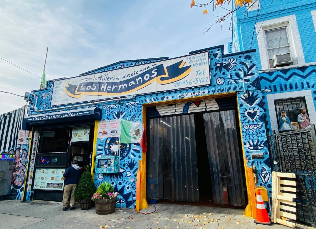 Bushwick Graffiti Tour La devanture colorée de la Tortilleria Mexicana Los Hermanos, avec une peinture murale vibrante et un drapeau mexicain à l'extérieur.