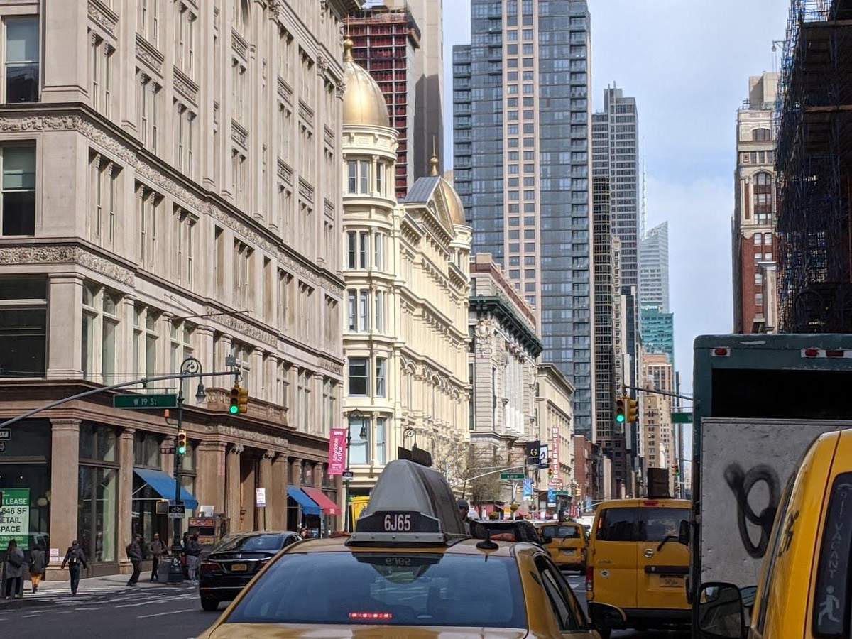 Visite guidée de Manhattan sur le thème de l'« Âge d'or » new-yorkais Une rue animée de la ville, avec des taxis, des piétons et de grands immeubles, dont un particulièrement somptueux, surmonté d'un dôme doré.