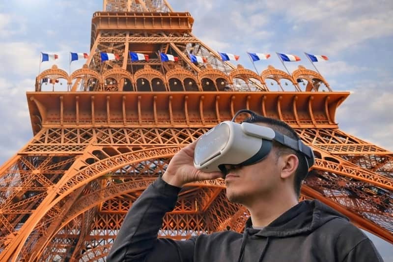 에펠탑: 가이드와 함께하는 VR 체험 VR 헤드셋을 착용한 사람이 부분적으로 흐린 하늘 아래 깃발로 장식된 에펠탑 근처에 서 있습니다.