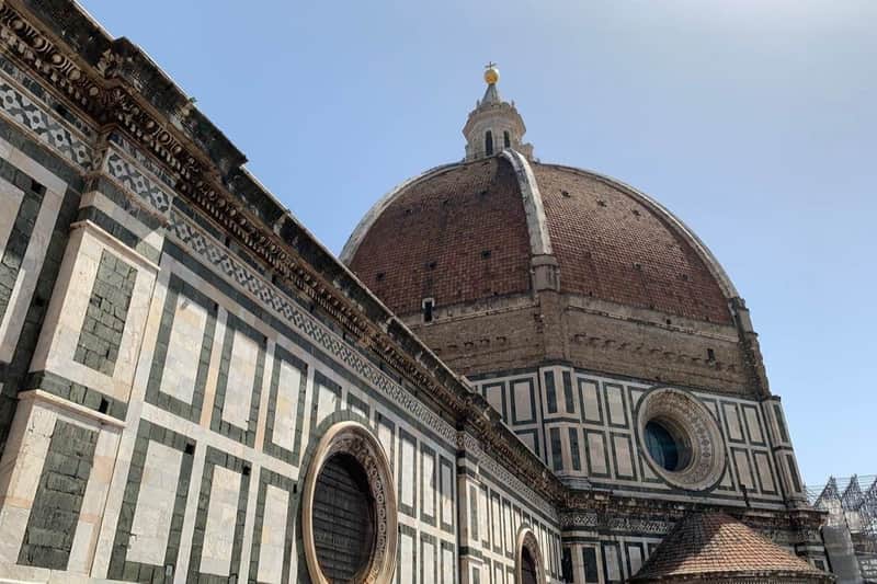 The dome of Florence's Cathedral with its marble facade and circular windows under a clear blue sky.