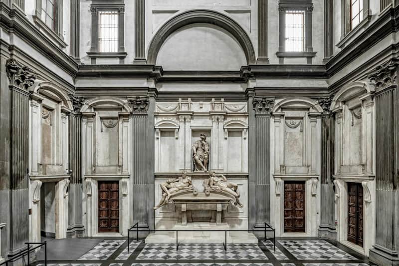 Interior of a historical building with decorative architecture, statues, and two wooden doors on either side.