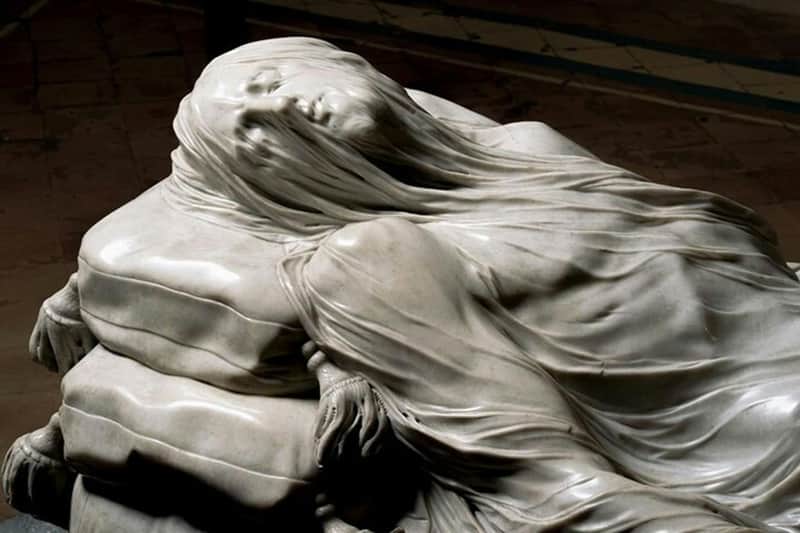 Statue de marbre représentant une figure drapée d'un voile délicat, présentant des détails complexes et réalistes.