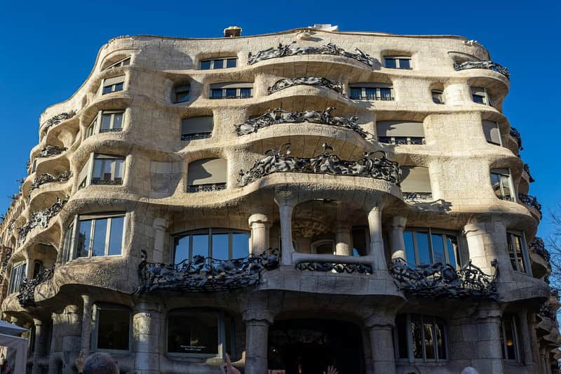澄んだ青い空の下で見られる、華やかな鉄工のバルコニーを備えた建物の波状の石のファサード。