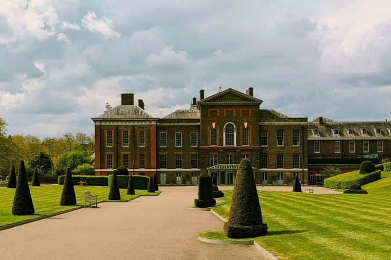 A historic building with brick and stone architecture surrounded by a landscaped garden with trimmed hedges and pathways.