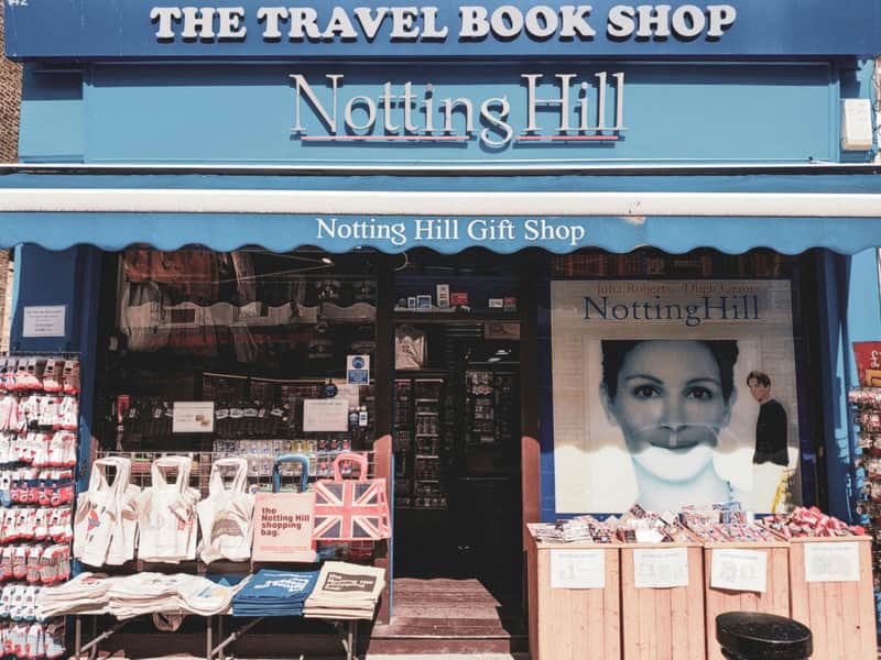 Storefront of "The Travel Book Shop" and "Notting Hill Gift Shop" with bags, books, and a large "Notting Hill" movie poster.