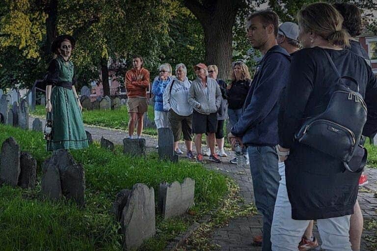 A group of people standing near gravestones in an outdoor setting with trees and grass.
