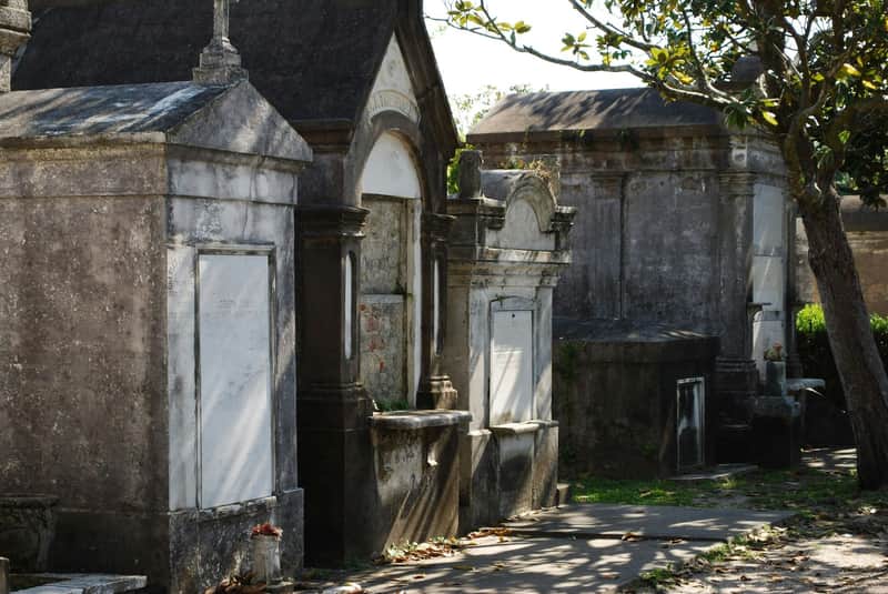Garden District: Guided Walking Tour A row of above-ground tombs in a cemetery, with stone facades and greenery surrounding them under a sunny sky.