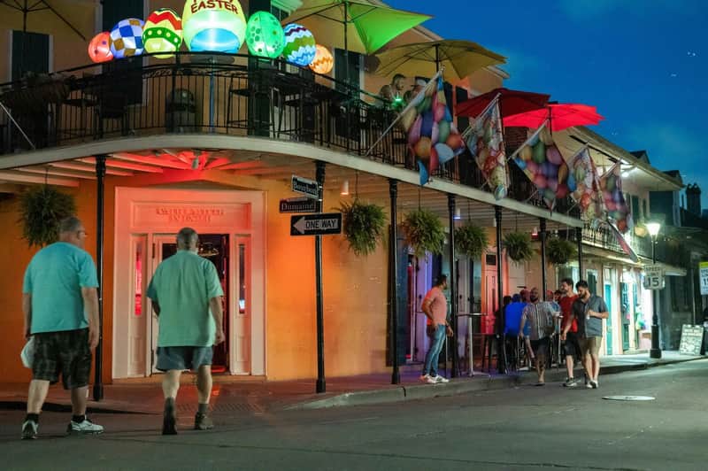 Visite de l'histoire LGBT Queer Des personnes marchant au coin d'une rue où se trouve un bâtiment très éclairé, décoré de lumières et de drapeaux colorés sur le thème de Pâques.
