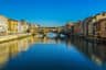A historic bridge over a calm river with buildings on both sides under a clear blue sky.