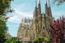 Sagrada Familia: Skip The Line Ticket + Guided Tour A large, intricate Gothic-style cathedral with multiple spires under a blue sky, surrounded by greenery and trees.